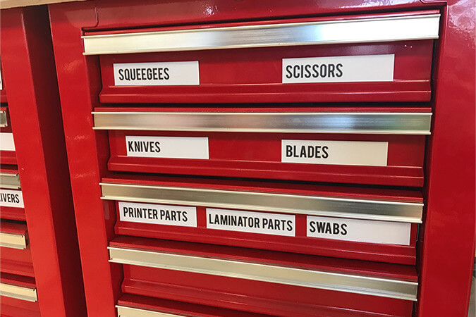 Red industrial tool cabinet with drawers labeled for squeegees, scissors, knives, blades, and repair parts